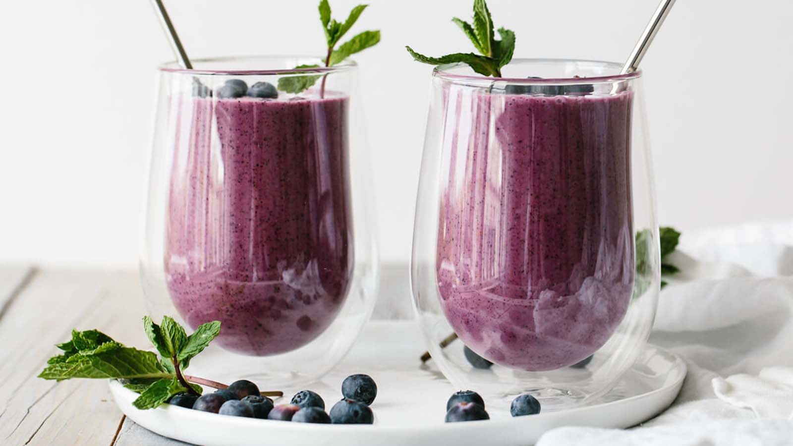 A deep purple healthy blended antioxidant blueberry smoothie inside a glass container cup.