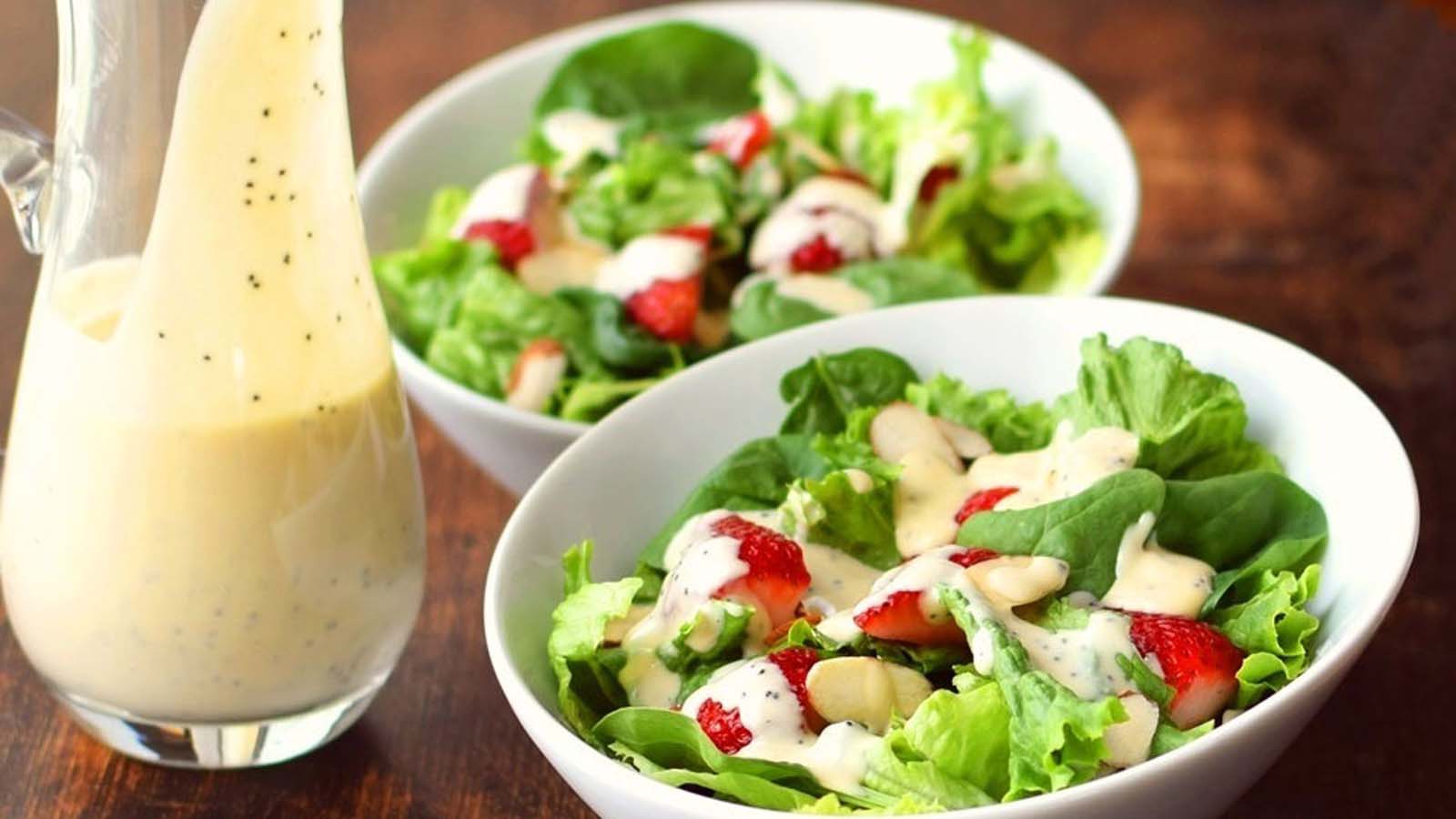 Creamy homemade salad dressing being poured from a small glass jar or pitcher.