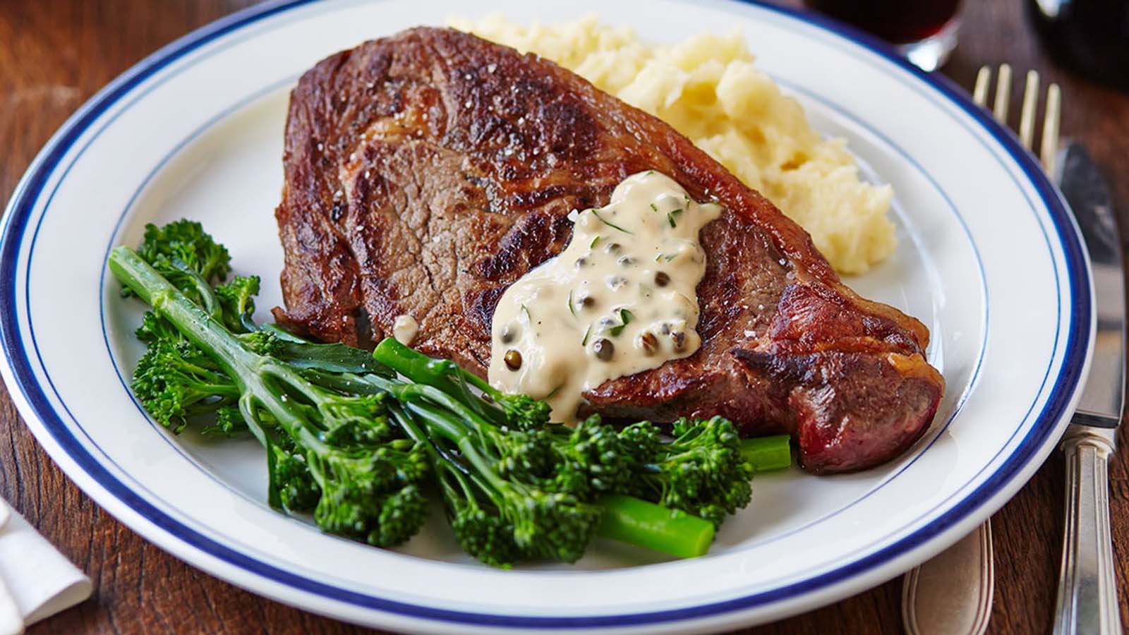 savoury green peppercorn steak sauce served in a gravy boat next to grilled meat.