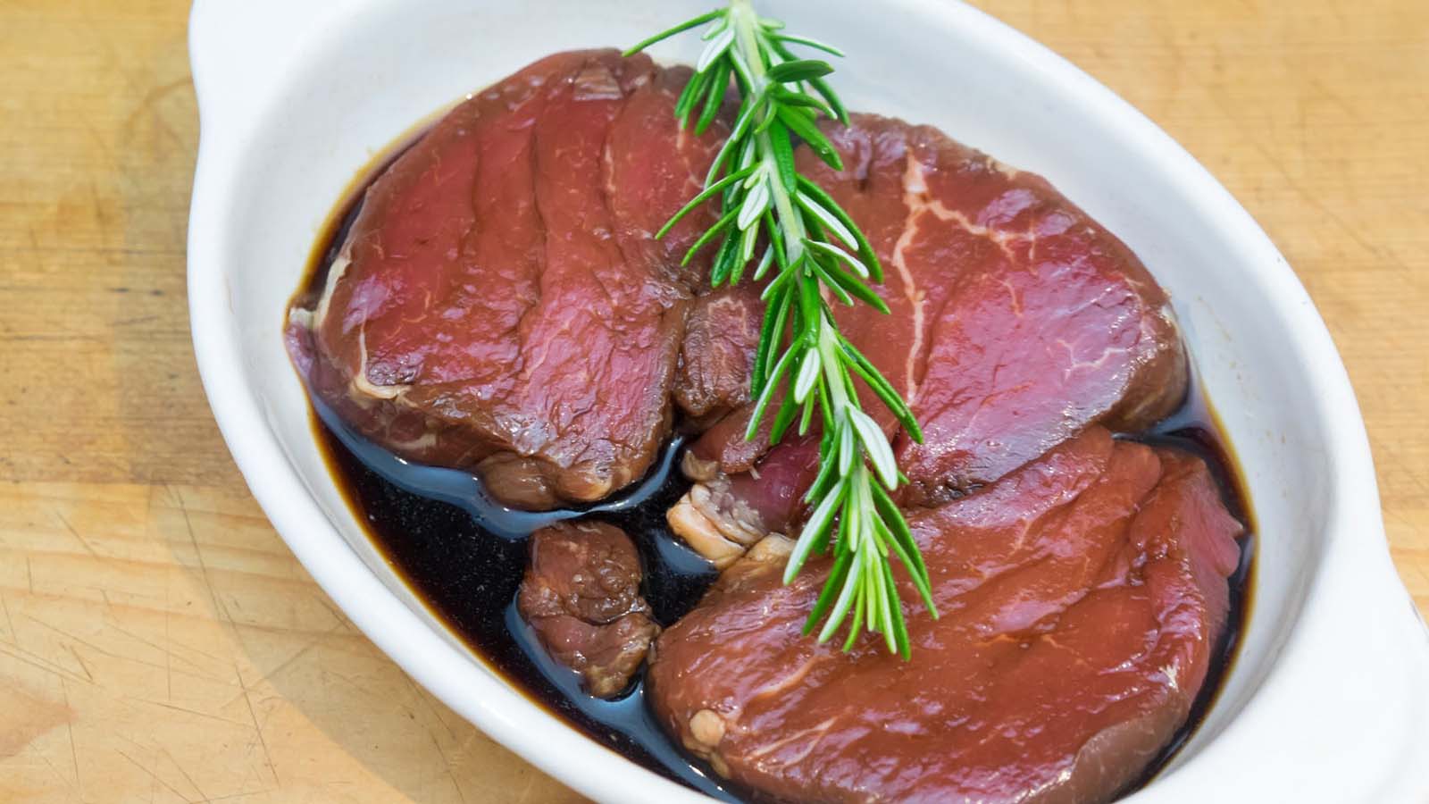 Raw beef steaks soaking in a dark, rich overnight marinade with garlic and herbs.