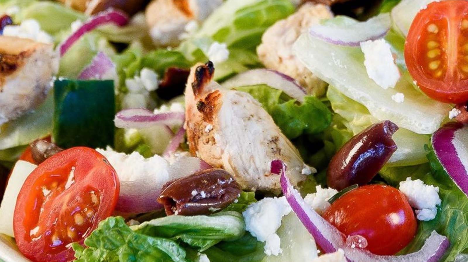 A healthy smoked chicken salad with tender pulled chicken strips over leafy greens.