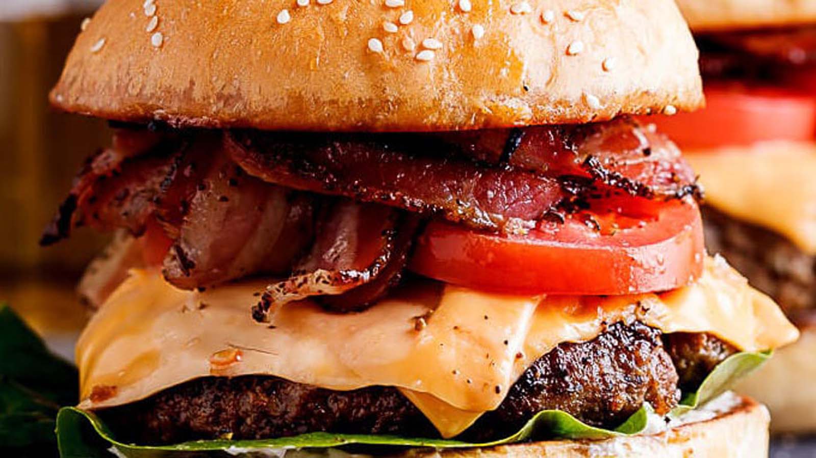 A juicy grilled beef hamburger with melting cheese, lettuce, and tomato on a brioche bun.