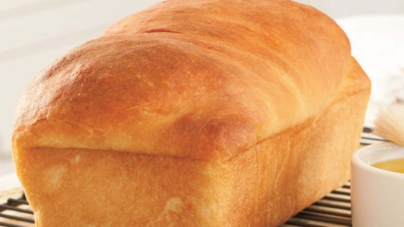 A freshly baked loaf of homemade crusty brown bread sliced on a wooden cutting board.