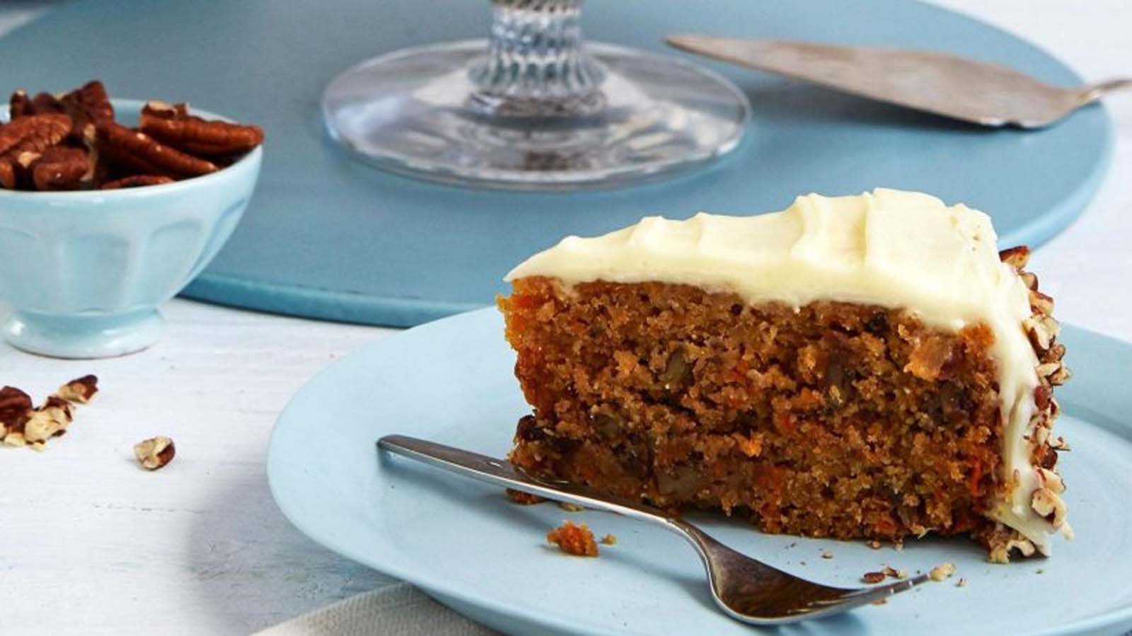 A slice of moist carrot cake layered with rich cream cheese frosting and chopped nuts.