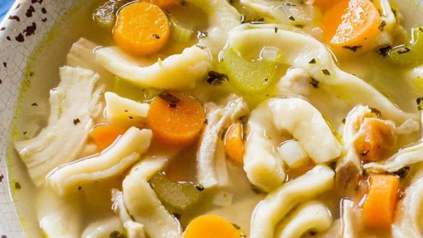 A comforting bowl of hot chicken noodle soup with clear broth and shredded chicken.