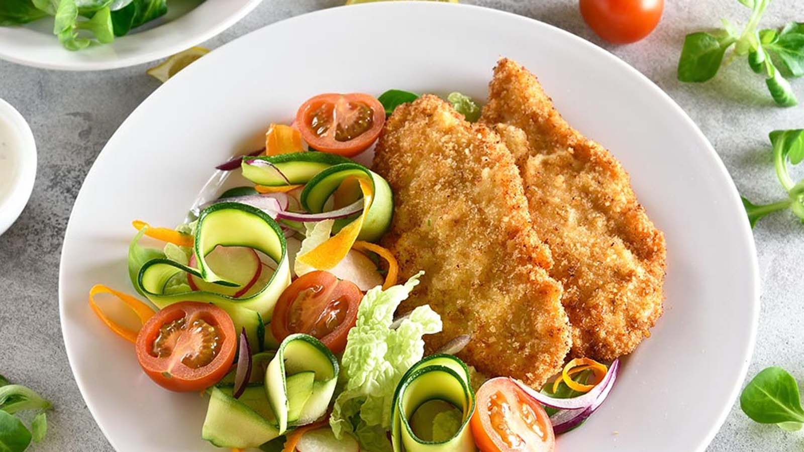 A golden brown, extra crispy pan-fried tender chicken schnitzel cutlet served on a plate.