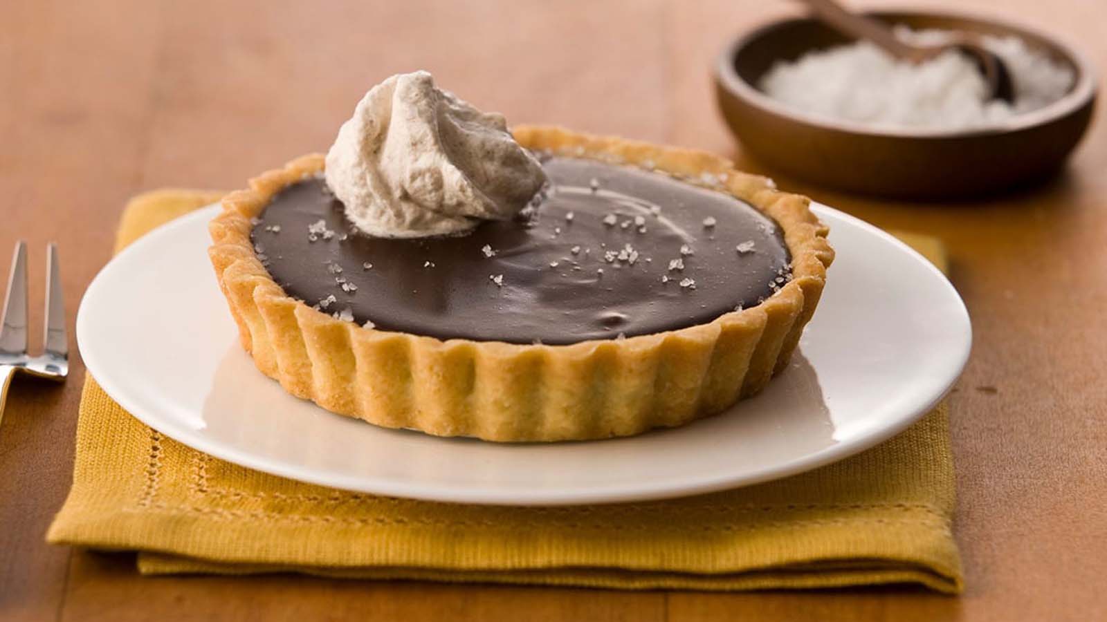 A sleek and glossy dark chocolate tart in a crisp pastry shell.