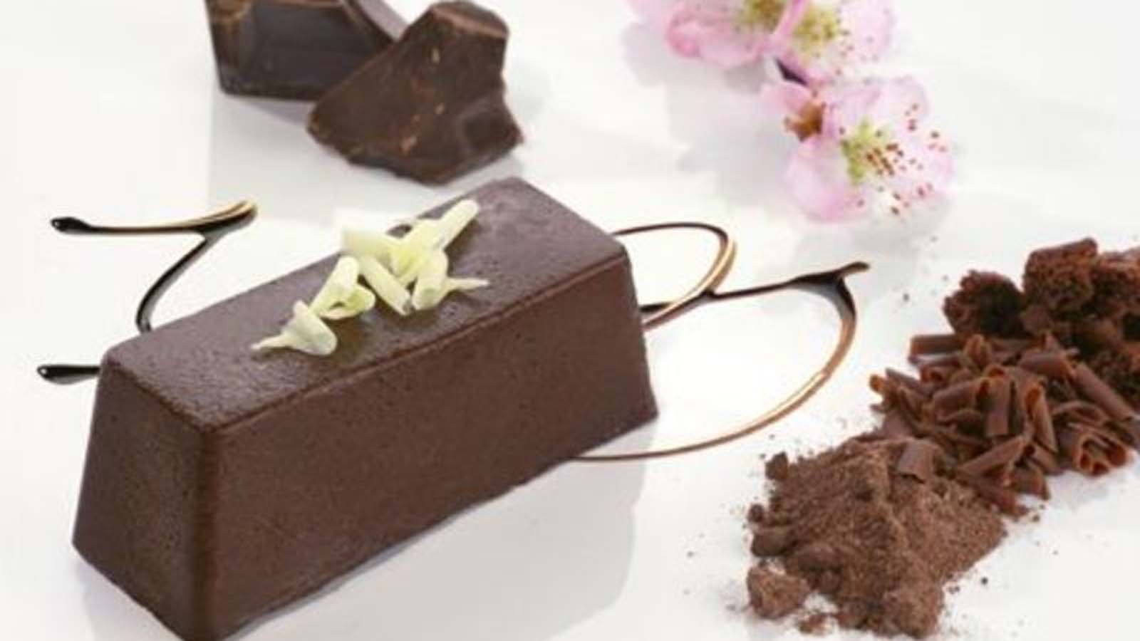 A dense and rich chocolate terrine dessert sliced on a modern serving board.