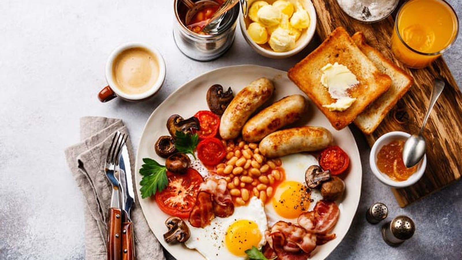 A full English breakfast platter with fried eggs, bacon, sausage, beans, and toast.