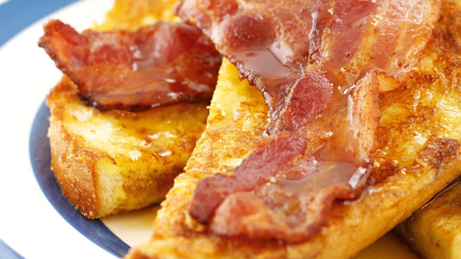 Thick slices of golden French toast served with crispy bacon slices and sweet maple syrup.