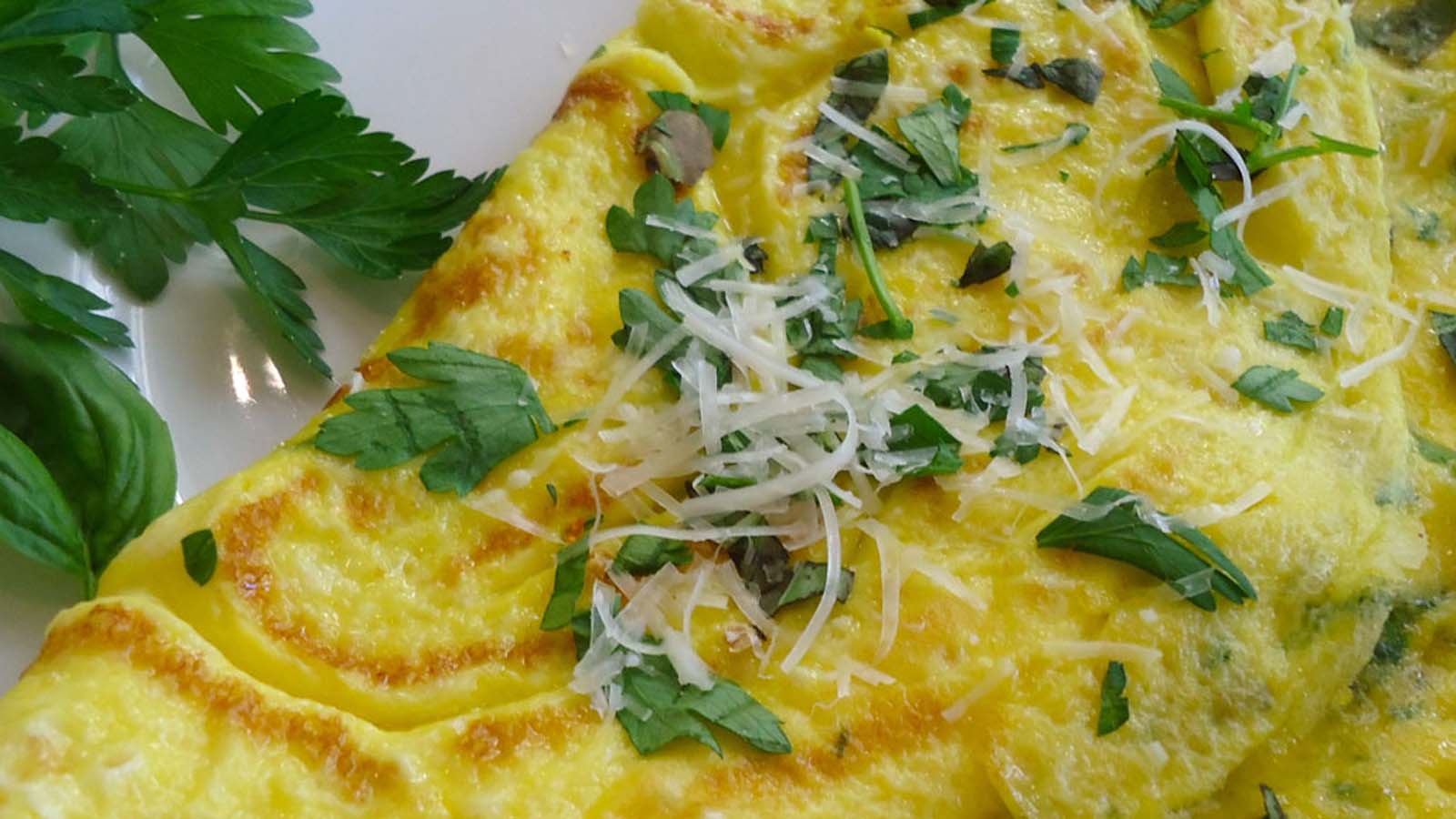 A fluffy breakfast herb omelet cooked to a light golden brown folded on a plate.