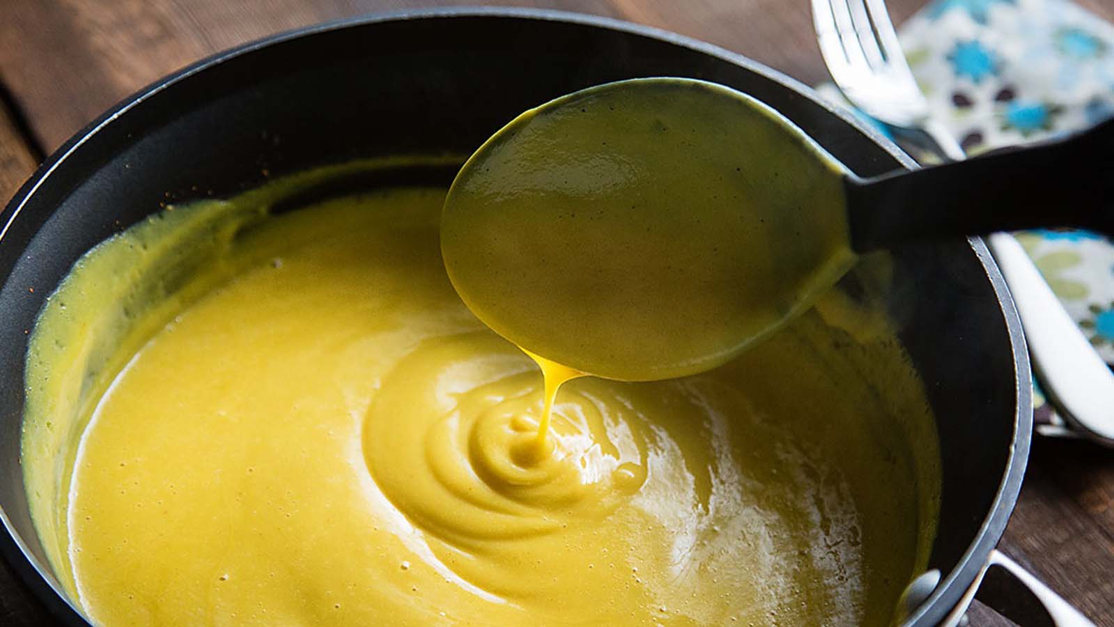 A velvety smooth, golden homemade cheddar cheese sauce pouring from a gravy boat.
