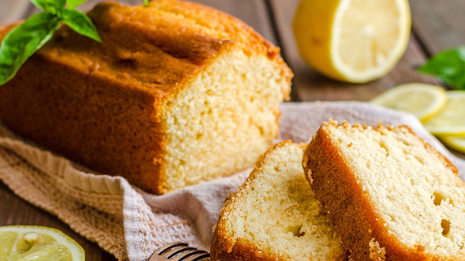 A beautiful sweet glazed lemon loaf cake sliced neatly on a kitchen cutting board.