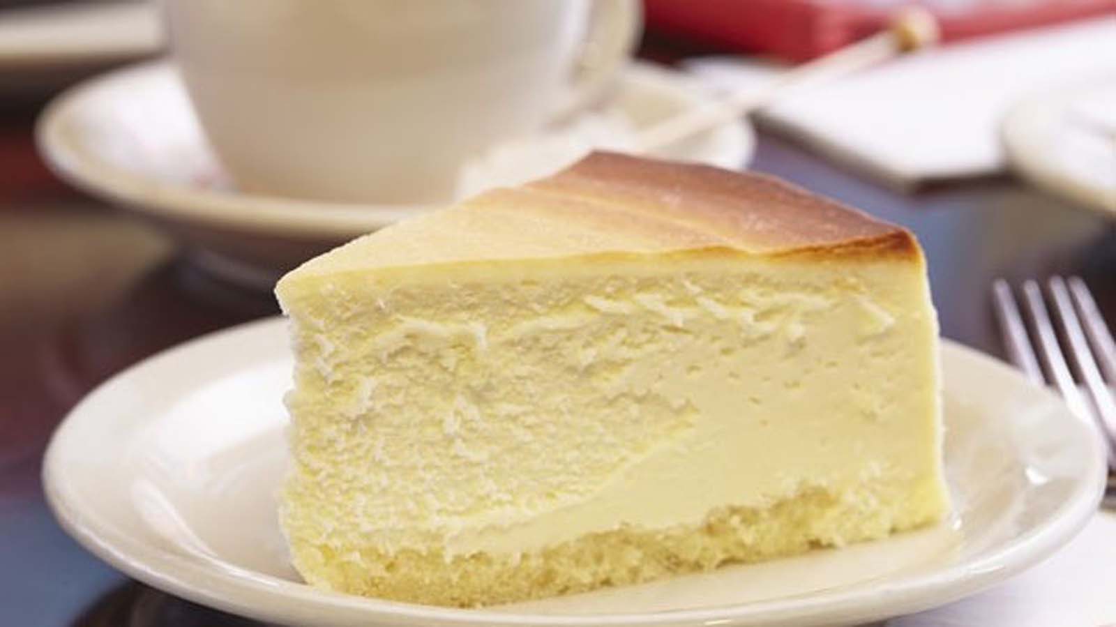 A dense, rich slice of authentic baked New York cheesecake on a plate.