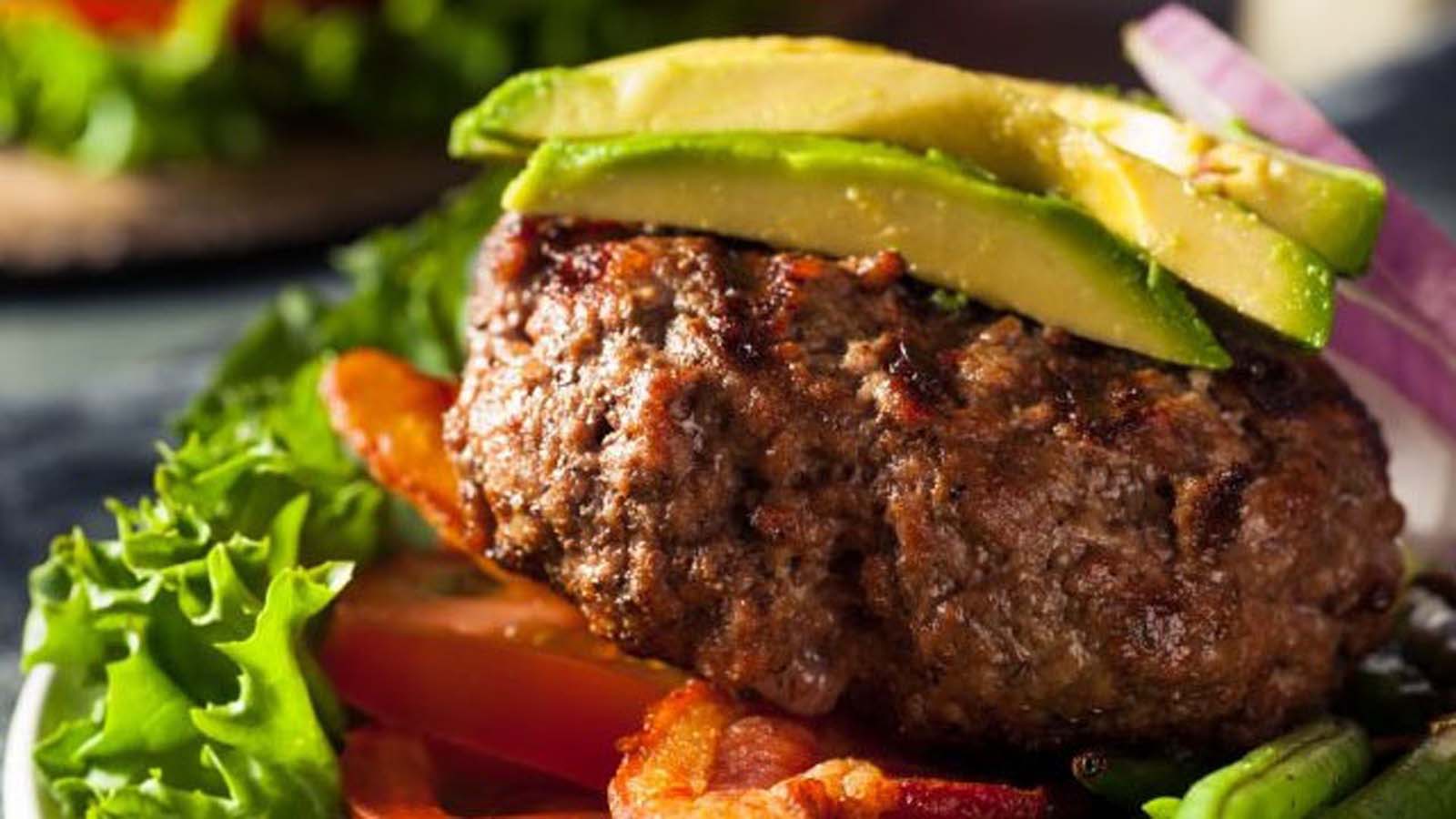 A lean and healthy gourmet ostrich hamburger stacked with fresh salad on a bun.