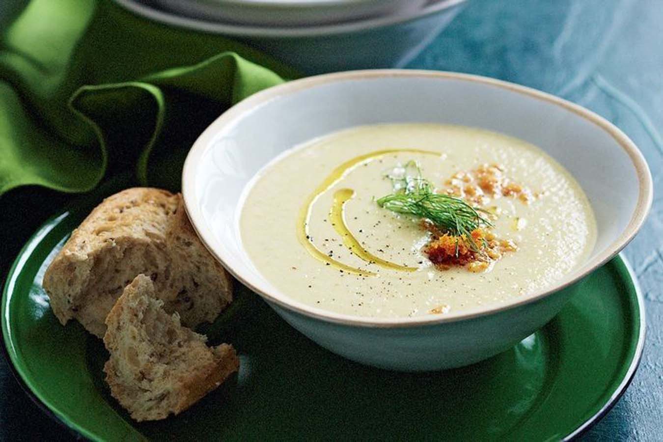 A comforting bowl of smooth, creamy pale white parsnip soup garnished with herbs.