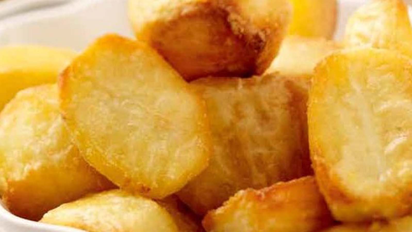 A plate of extra crispy, golden brown perfect roast potatoes seasoned with rosemary.