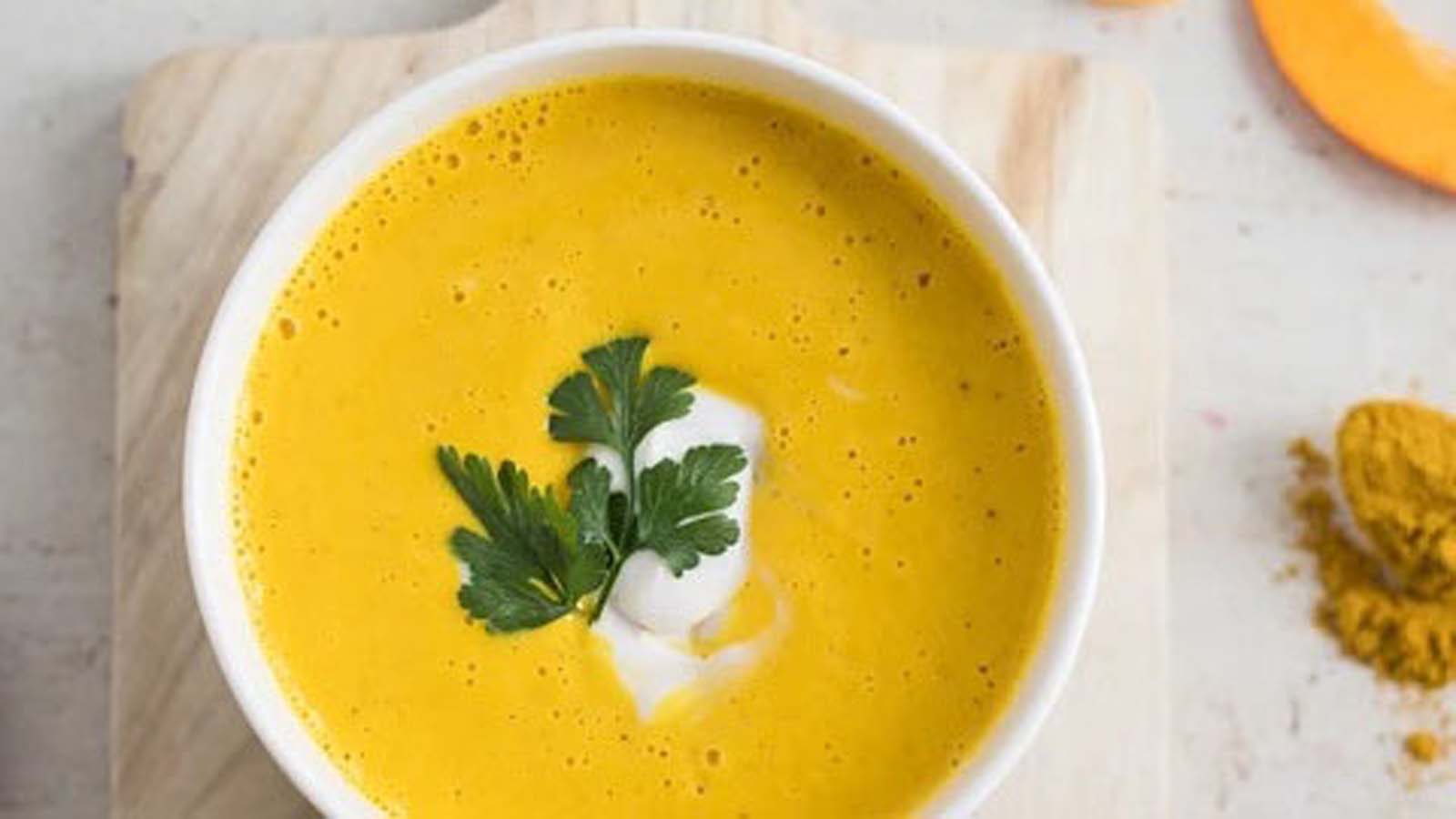 A warm, comforting bowl of thick golden pumpkin soup garnished with cream swirls.