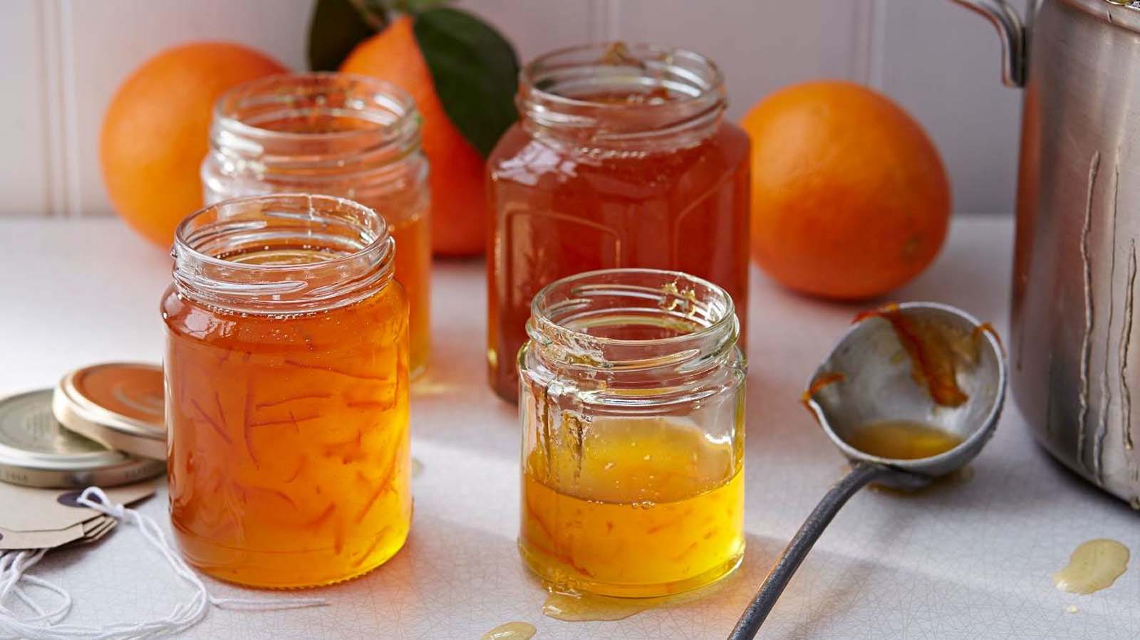 A jar of thick, glassy bitter sweet Seville orange marmalade jam showing citrus rinds.
