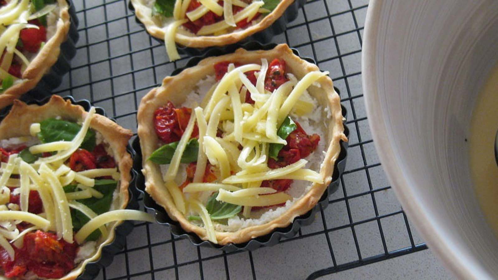 A vibrant vegetarian quiche baked with sun-dried tomatoes, fresh basil leaves, and crumbled feta cheese.