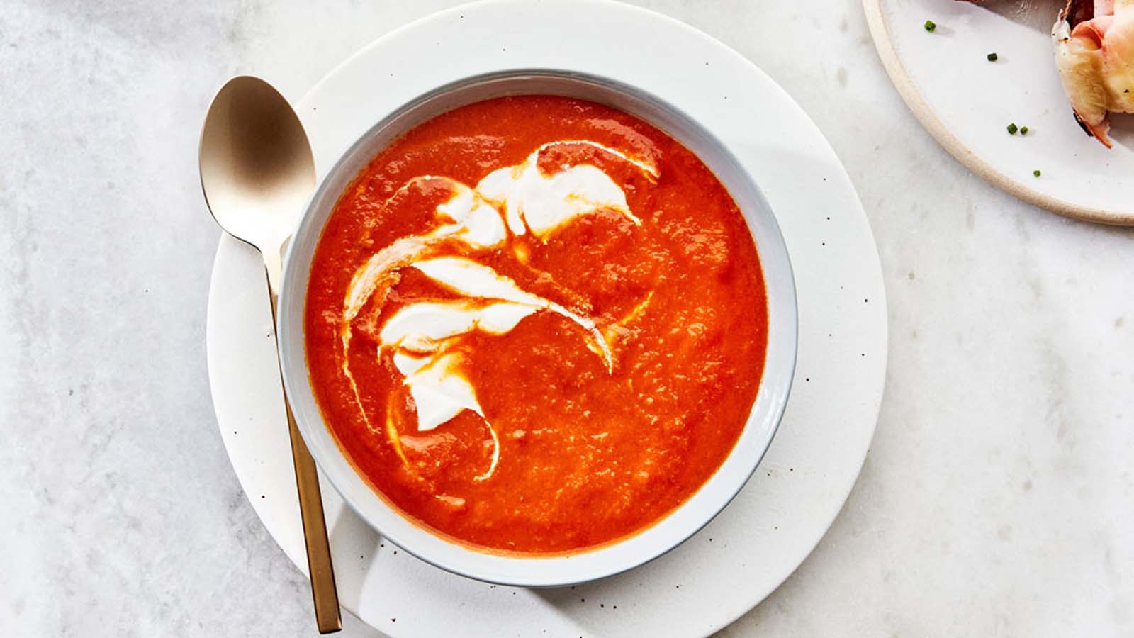 A classic, vibrant smooth tomato soup served hot in a deep soup bowl.
