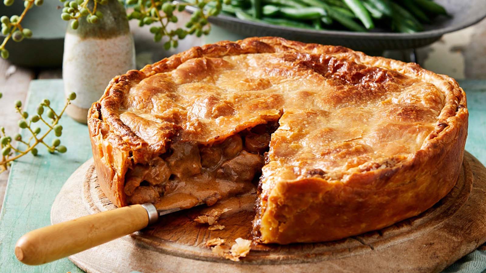 A hearty, golden brown baked venison pie with a flaky puff pastry lid shell.