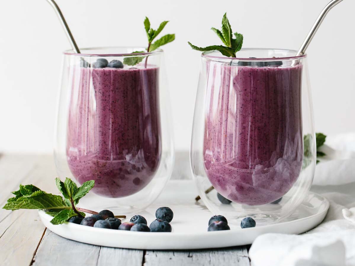 A deep purple healthy blended antioxidant blueberry smoothie inside a glass container cup.