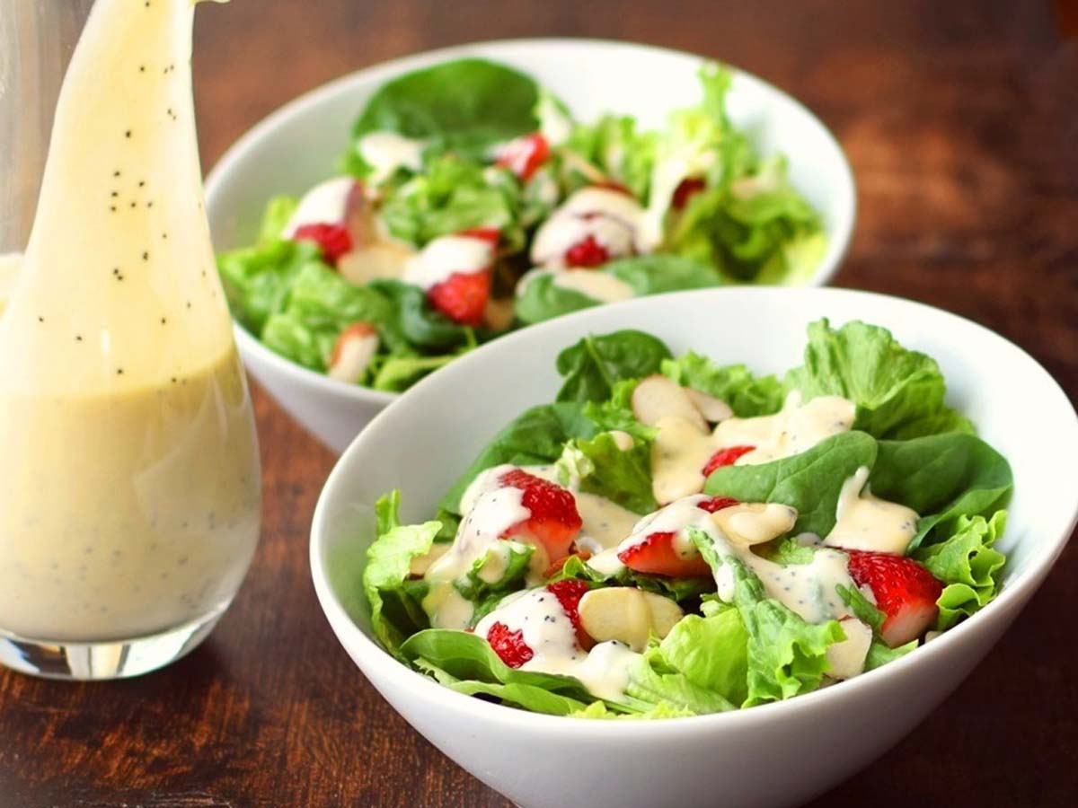 Creamy homemade salad dressing being poured from a small glass jar or pitcher.