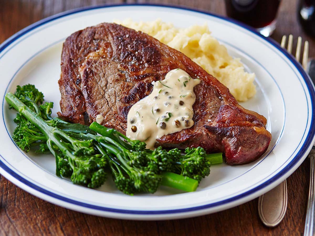 savoury green peppercorn steak sauce served in a gravy boat next to grilled meat.