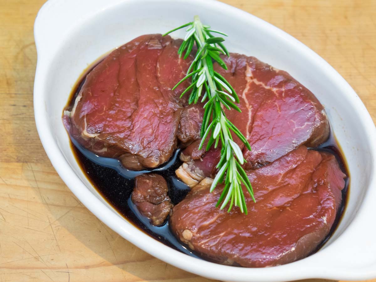 Raw beef steaks soaking in a dark, rich overnight marinade with garlic and herbs.