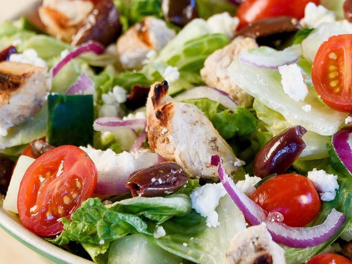 A healthy smoked chicken salad with tender pulled chicken strips over leafy greens.