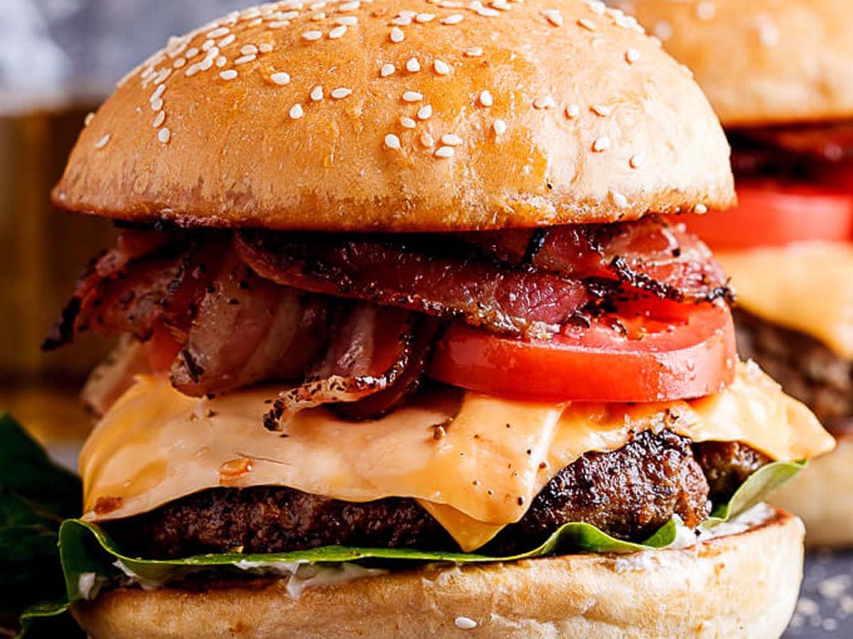 A juicy grilled beef hamburger with melting cheese, lettuce, and tomato on a brioche bun.
