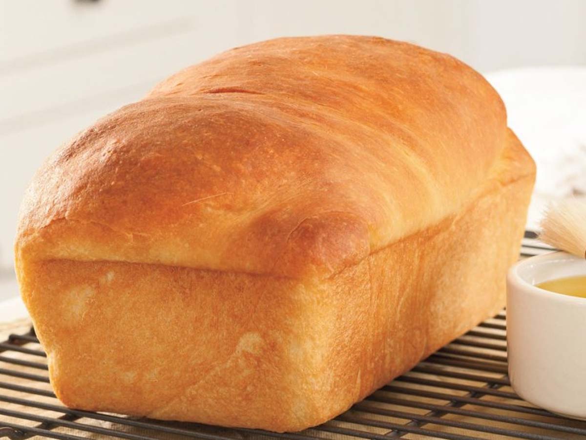 A freshly baked loaf of homemade crusty brown bread sliced on a wooden cutting board.