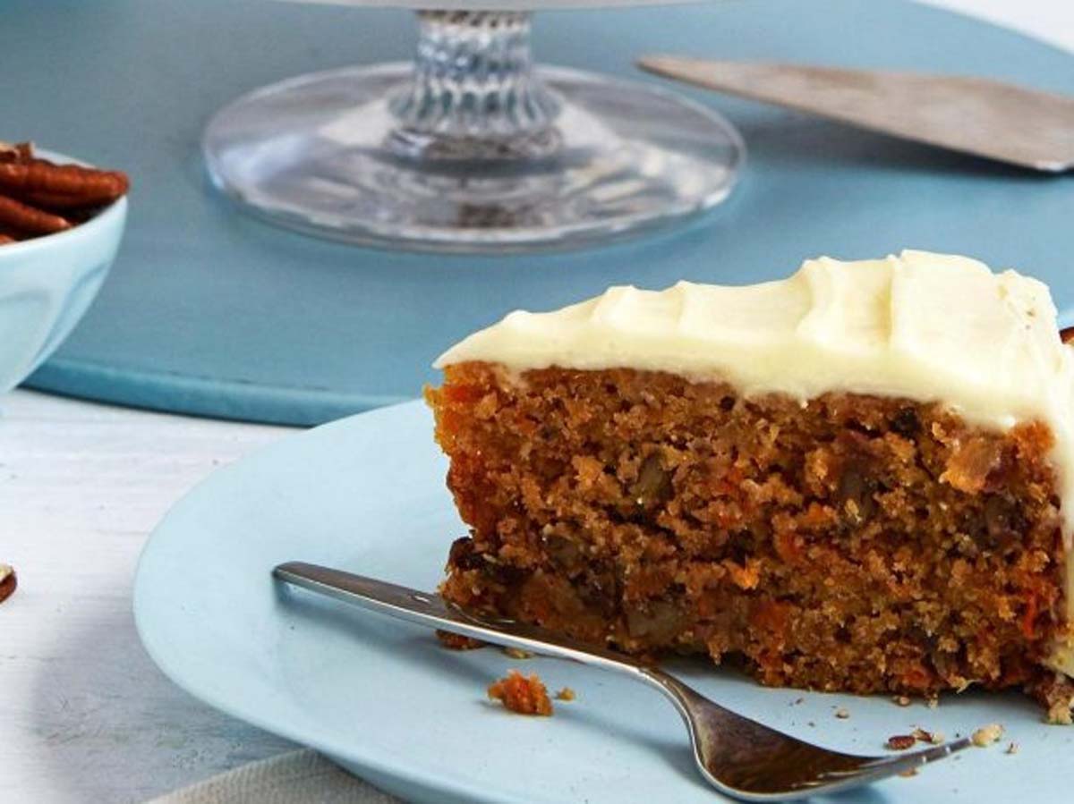 A slice of moist carrot cake layered with rich cream cheese frosting and chopped nuts.