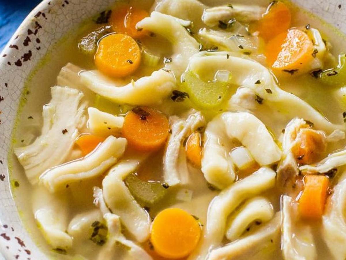 A comforting bowl of hot chicken noodle soup with clear broth and shredded chicken.