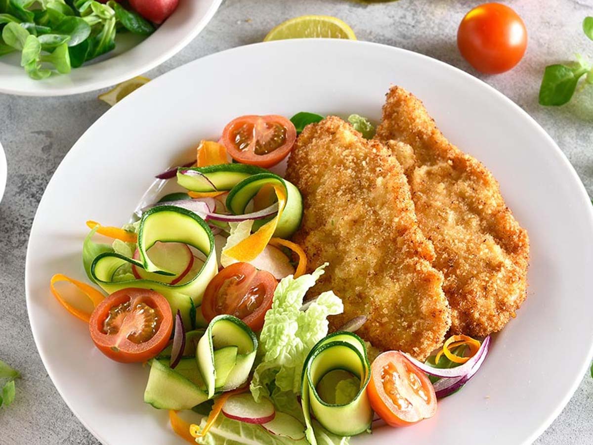 A golden brown, extra crispy pan-fried tender chicken schnitzel cutlet served on a plate.