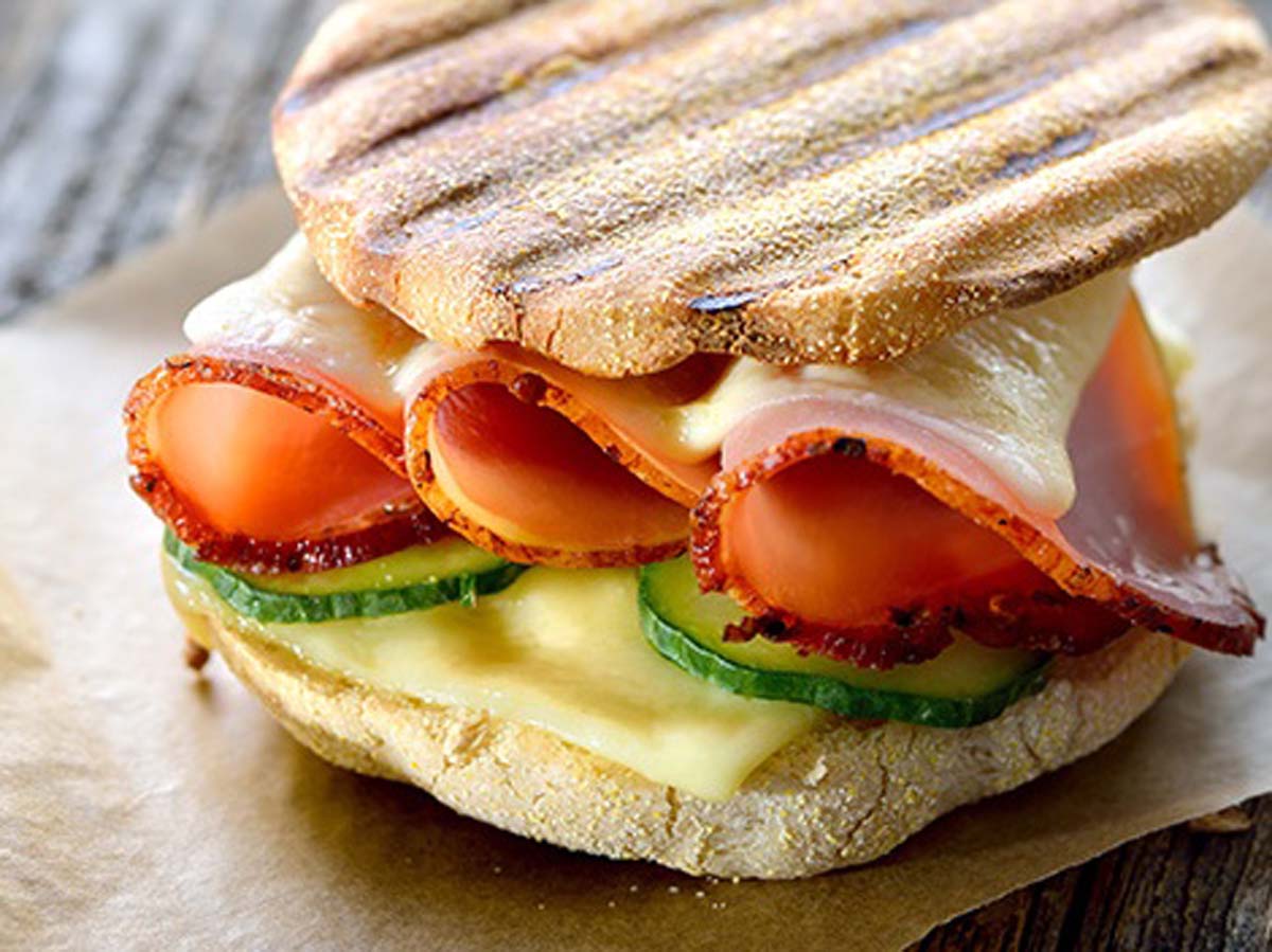A perfectly toasted Italian panini sandwich filled with melting cheese, tomato, and ham.