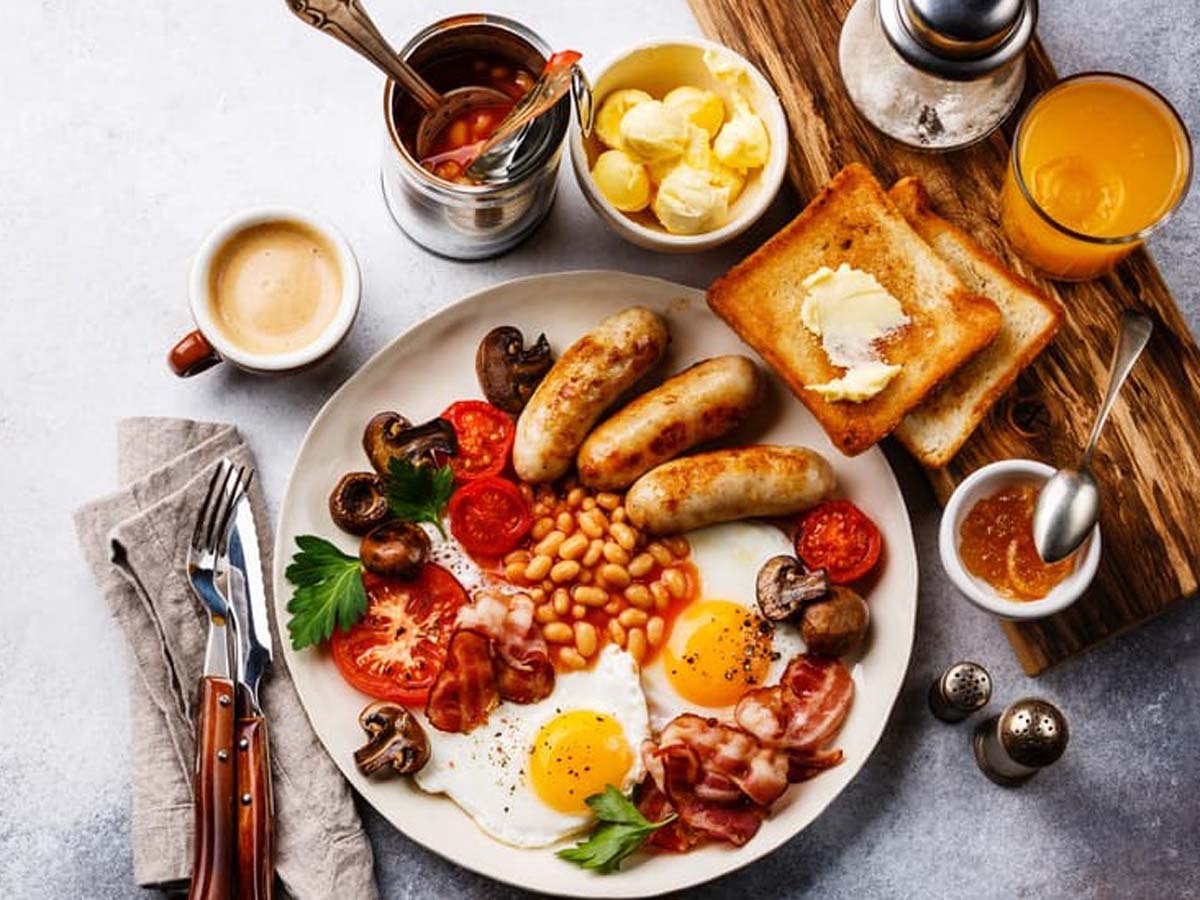 A full English breakfast platter with fried eggs, bacon, sausage, beans, and toast.