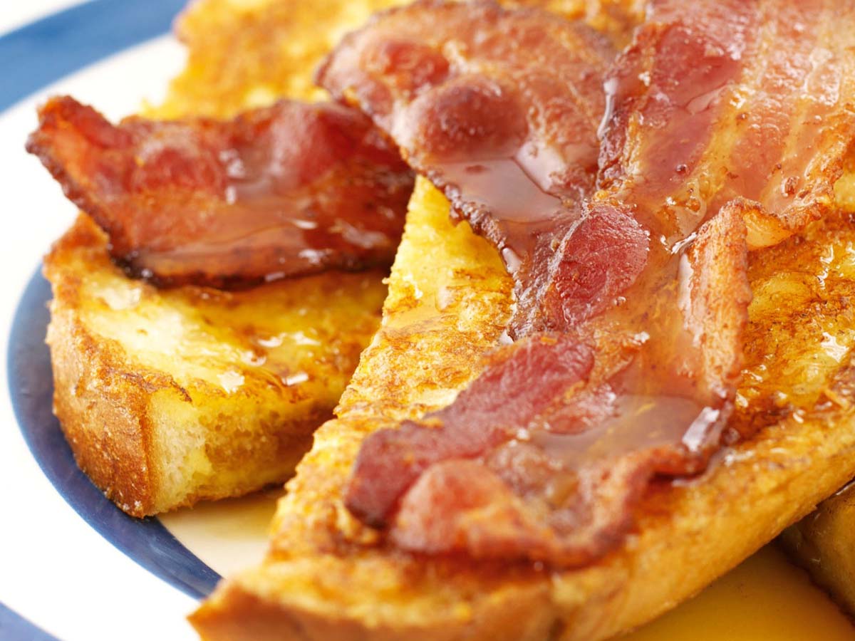Thick slices of golden French toast served with crispy bacon slices and sweet maple syrup.
