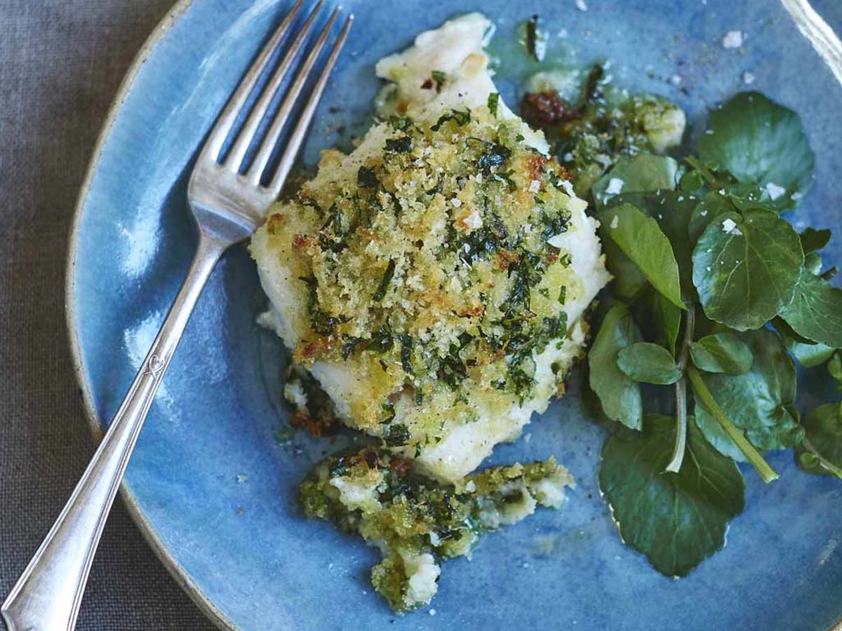 A fresh green herb crust mix pressed onto a white fish fillet for baking.