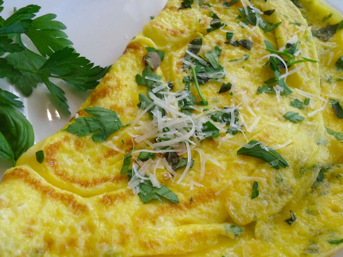 A fluffy breakfast herb omelet cooked to a light golden brown folded on a plate.