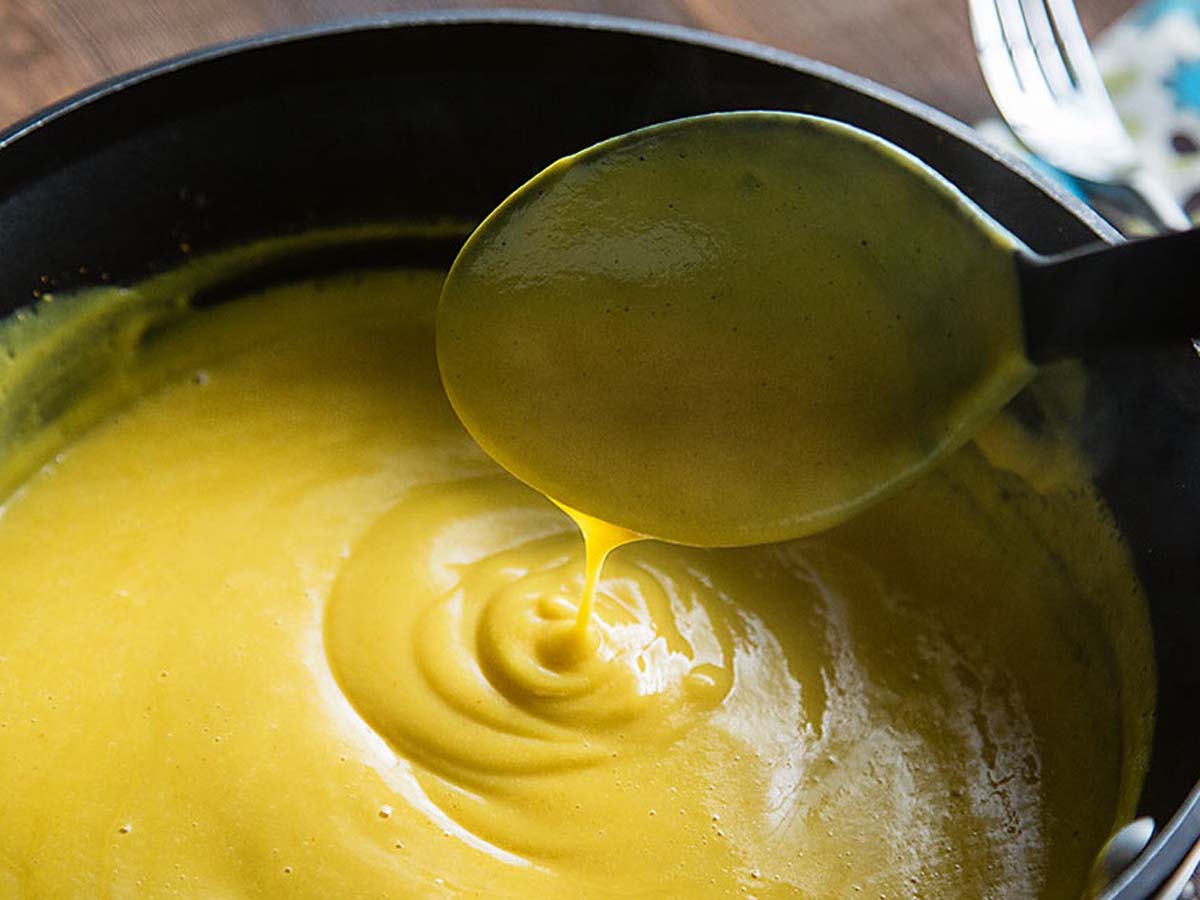 A velvety smooth, golden homemade cheddar cheese sauce pouring from a gravy boat.