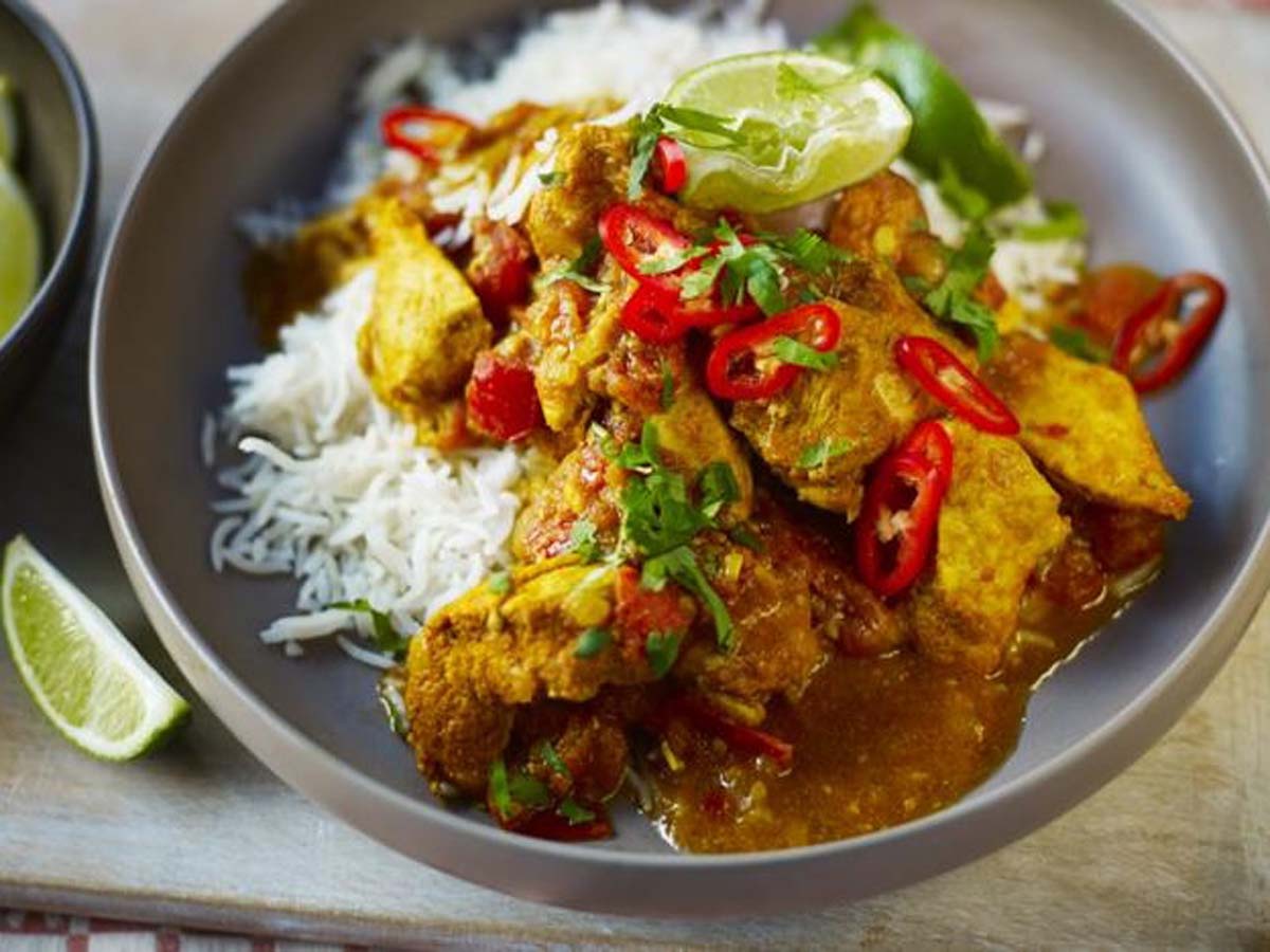 An aromatic Indian chicken curry served alongside a bed of bright yellow saffron rice.