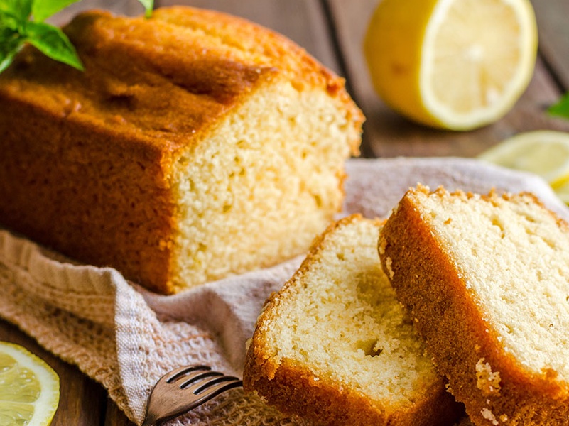 A beautiful sweet glazed lemon loaf cake sliced neatly on a kitchen cutting board.