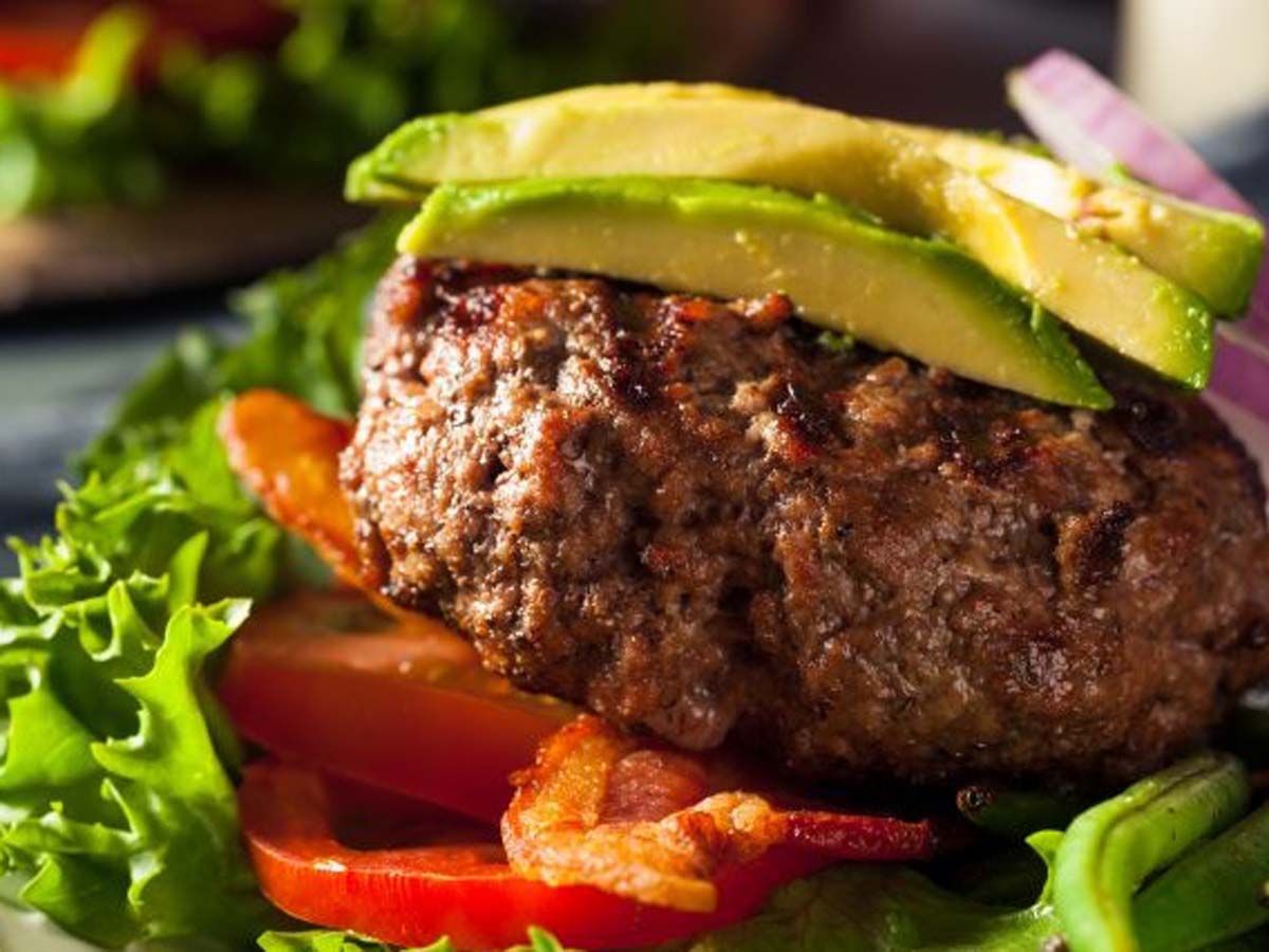 A lean and healthy gourmet ostrich hamburger stacked with fresh salad on a bun.