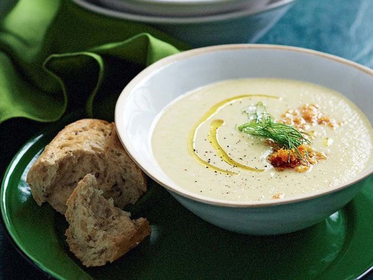 A comforting bowl of smooth, creamy pale white parsnip soup garnished with herbs.