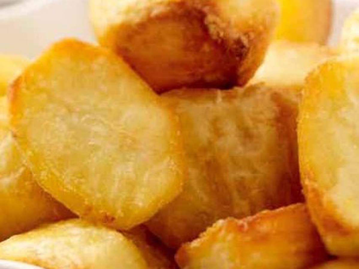 A plate of extra crispy, golden brown perfect roast potatoes seasoned with rosemary.
