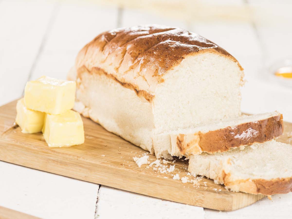 A golden loaf of sliced plain white homemade bread fresh from the oven.