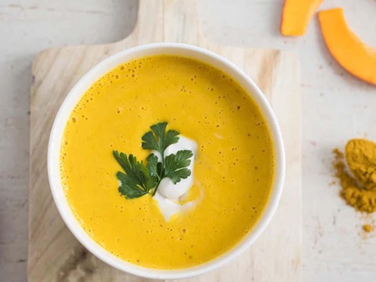 A warm, comforting bowl of thick golden pumpkin soup garnished with cream swirls.