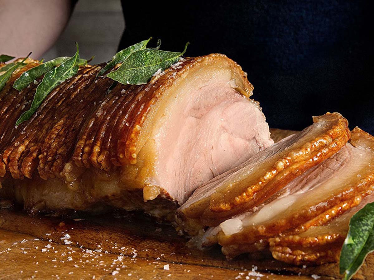 A succulent cut of roast pork roast showing perfect crispy crackling skin on top.